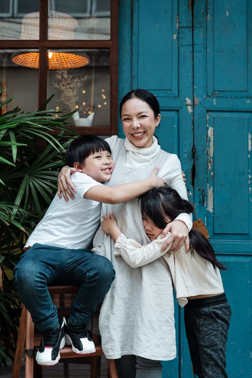 photo of woman hugging her children while smiling